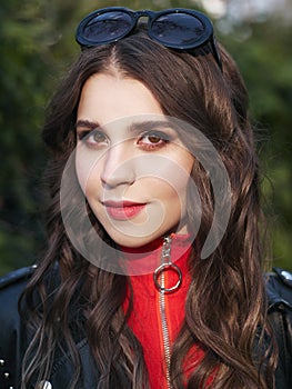 Closeup portrait of young brown-haired curly woman with trendy creative red makeup posing outdoors in bright sunlight. Pretty girl