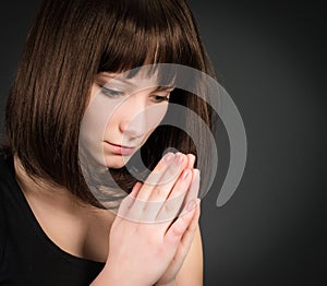 Closeup portrait of a young brunette woman praying. Praying girl on dark background.