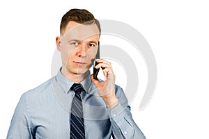 Closeup portrait of young businessman dressed in blue shirt and tie, talking on the mobile phone, isolated on white background