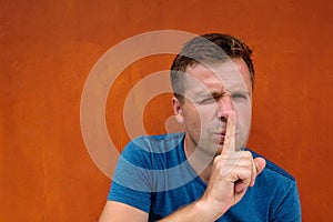 Closeup portrait of young caucasian man placing finger on lips as if to say, shh, be quiet