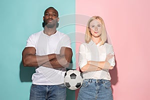 Closeup portrait of young couple, man, woman with football ball. They are serious, concerned on pink and blue background