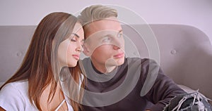 Closeup portrait of young cute caucasian couple being affectionate hugging and looking at camera sitting together