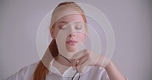 Closeup portrait of young cute caucasian redhead female looking at camera holding her glasses with thoughtfulness