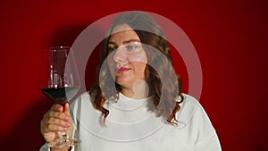 Closeup portrait of young female customer drinking red wine on red background. Wine expert tasting, rating and drinking