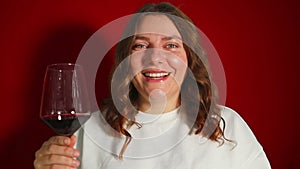 Closeup portrait of young female customer drinking red wine on red background. Wine expert tasting, rating and drinking