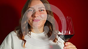 Closeup portrait of young female customer drinking red wine on red background. Wine expert tasting, rating and drinking