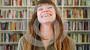 Closeup portrait of a young female student smiling and laughing while standing in a library at university. Face of a