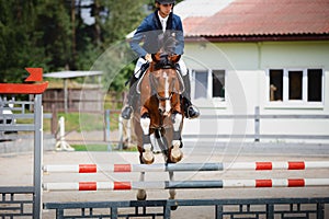 Young gelding horse and adult man rider jumping during equestrian showjumping competition in daytime photo
