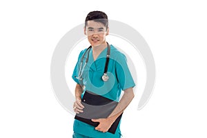 Closeup portrait of young handsome brunette man doctor in blue uniform with stethoscope and board in hands looking at