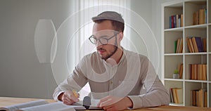 Closeup portrait of young handsome caucasian male student in eyeglasses studying and using the tablet in the college