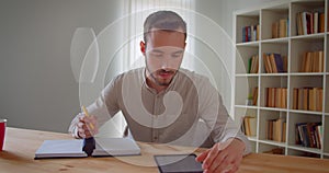 Closeup portrait of young handsome caucasian male student studying and using the tablet looking at camera smiling