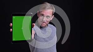 Closeup portrait of young handsome caucasian man using the tablet and showing green chroma screen to camera.