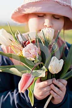 Closeup portrait of a young happy preteen girl holding a bunch of tulips and smelling the flowers