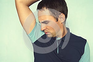 Closeup portrait of young man, smelling, sniffing his armpit, something stinks, very bad, foul odor situation, on blue wall backgr