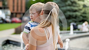 Closeup portrait of young mother hugging and caressing her crying little child boy in park