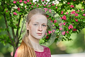 Closeup portrait of young natural beautiful redhead woman in fuchsia blouse posing against blossoming tree with blurred green foli