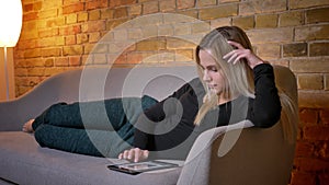 Closeup portrait of young pretty housewife using the tablet and lying on the sofa laidback indoors at cozy home