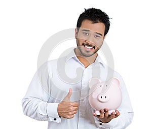 Portrait of young smiling student, worker man holding piggy bank, giving thumbs up