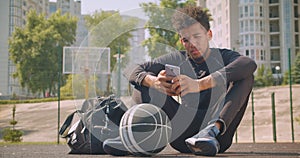 Closeup portrait of young strong African American male basketball player texting on the phone and looking at camera