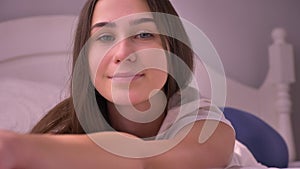 Closeup portrait of young stunning caucasian female lying on the bed and looking at camera smiling