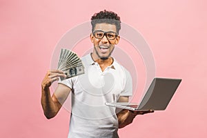 Closeup portrait, young successful african american business man making money from internet, holding cash in hand, laptop in