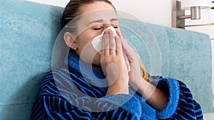 Closeup portrait of young woman feeling unwell blowing nose in paper tissue