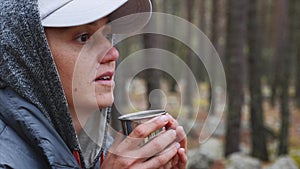 Closeup portrait of young woman hiker drinking tea from metal cup in forest.