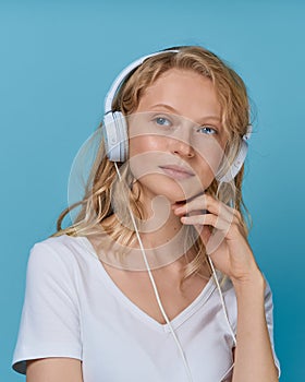 Closeup portrait of young woman listening music via headphones on color bright blue tone wall