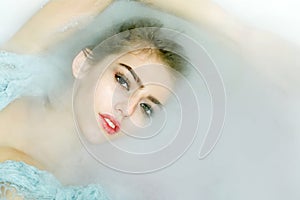 Closeup portrat of young sexy girl with wet hair lying in white bathtub full of water and soap foam