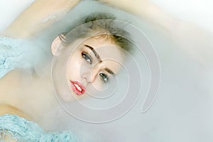 Closeup portrat of young sexy girl with wet hair lying in white bathtub full of water and soap foam photo