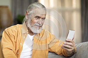 Closeup of positive old man using mobile phone at home