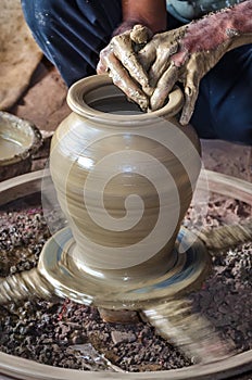 Closeup of potter`s hands making clay water pot on pottery wheel.