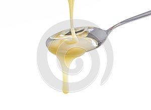 Closeup pouring condensed milk with teaspoon on white background