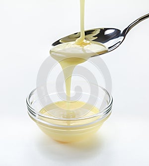 Closeup pouring condensed milk with teaspoon on white background