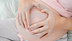 Closeup of pregnant woman hands making heart shape on big belly. Concept of expecting child, love and parenting.