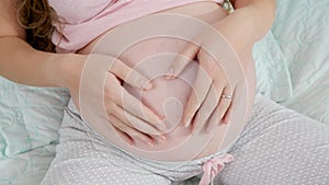 Closeup of pregnant woman hands making heart shape on big belly. Concept of expecting child, love and parenting.