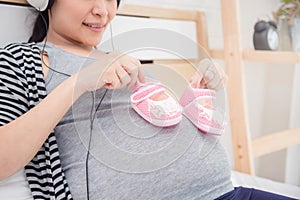 Closeup of pregnant woman holding baby shoes on her belly and smiles
