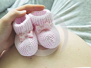 Closeup of pregnant woman holding pink baby booties on her belly