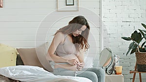 Closeup pregnant woman measuring her belly centimeters tape in bed.