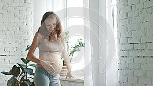 Closeup pregnant woman touching belly. Expecting mother standing window at home.