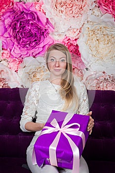 Closeup pretty blond woman looks at camera holding in hands big purple gift box