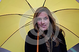 Closeup of pretty and elegant girl with a yellow umbrella looking intensely and interestingly at the camera