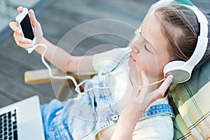 Closeup of pretty teen girl in headphones listening to music using a laptop outside on the terrace in the garden