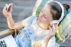 Closeup of pretty teen girl in headphones listening to music using a laptop outside on the terrace in the garden