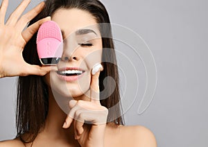 Closeup of pretty woman with pink face exfoliator brush silicone cleansing device for skin and cream and enjoys softness