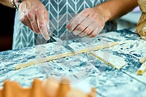 Closeup process making homemade pasta. Chef cook cutting with knife fresh dough for italian traditional pasta to thin ribbon.