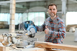 Closeup professional carpenter hold electric circular saw at sawmill. Skilled joiner using circular saw for cutting wood