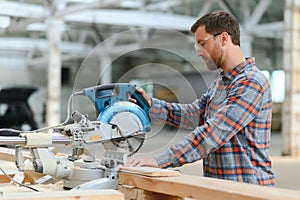 Closeup professional carpenter hold electric circular saw at sawmill. Skilled joiner using circular saw for cutting wood