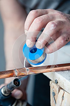 Closeup professional master plumber holding flux paste for soldering and brazing seams of copper pipe gas burner. Concept