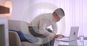 Closeup profile portrait of adult tired caucasian businessman using laptop sitting laidback on couch in apartment